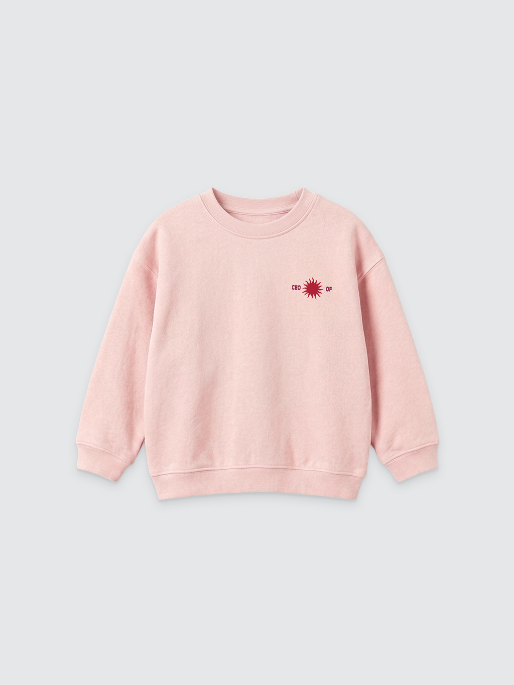 Ein hellrosa Kinder-Sweatshirt mit Rundhalsausschnitt und überschnittenen Schultern auf hellem Hintergrund. Auf der linken Brustseite befindet sich eine kleine dunkelrote Grafik, die eine Sonne zeigt, flankiert von dem Text „CEO OF“.