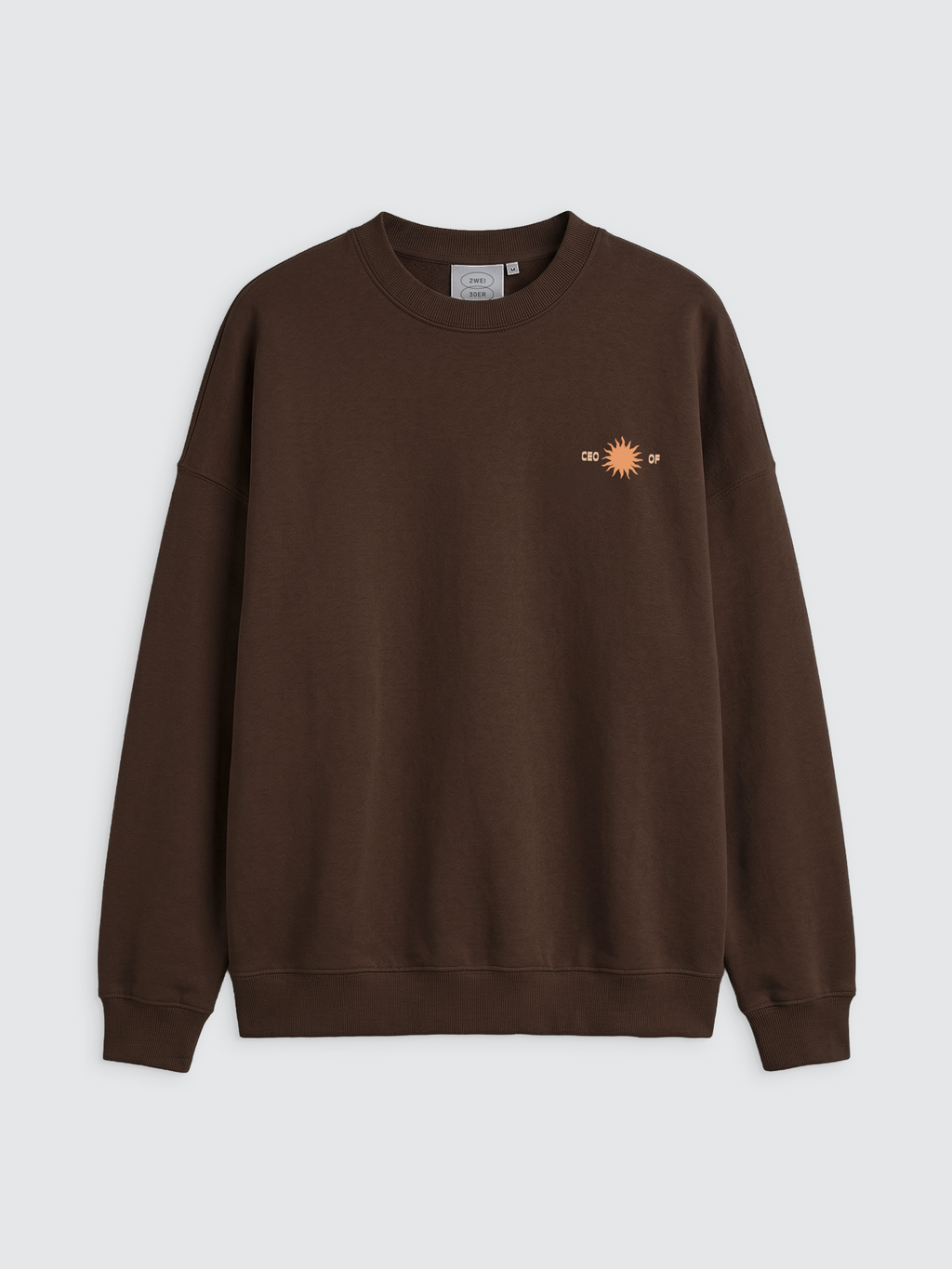Vorderansicht eines dunkelbraunen Oversize-Sweatshirts mit Rundhalsausschnitt und Rippbündchen an Ärmeln und Saum. Auf der linken Brustseite befindet sich ein kleiner, pfirsichfarbener Print einer Sonne, der von dem Schriftzug „CEO OF“ in derselben Farbe eingerahmt wird. Das Sweatshirt hat eine lockere Passform mit überschnittenen Schultern.