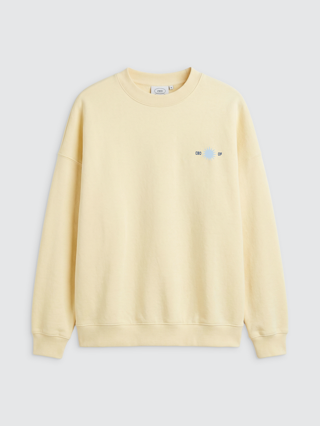 Vorderansicht eines hellgelben Oversize-Sweatshirts mit Rundhalsausschnitt und elastischen Rippbündchen. Auf der linken Brustseite befindet sich ein kleiner, hellblauer Print einer Sonne, der von dem dunkelblauen Schriftzug „CEO OF“ eingefasst wird. Das Sweatshirt hat eine lockere, moderne Passform mit tief angesetzten Schultern.
