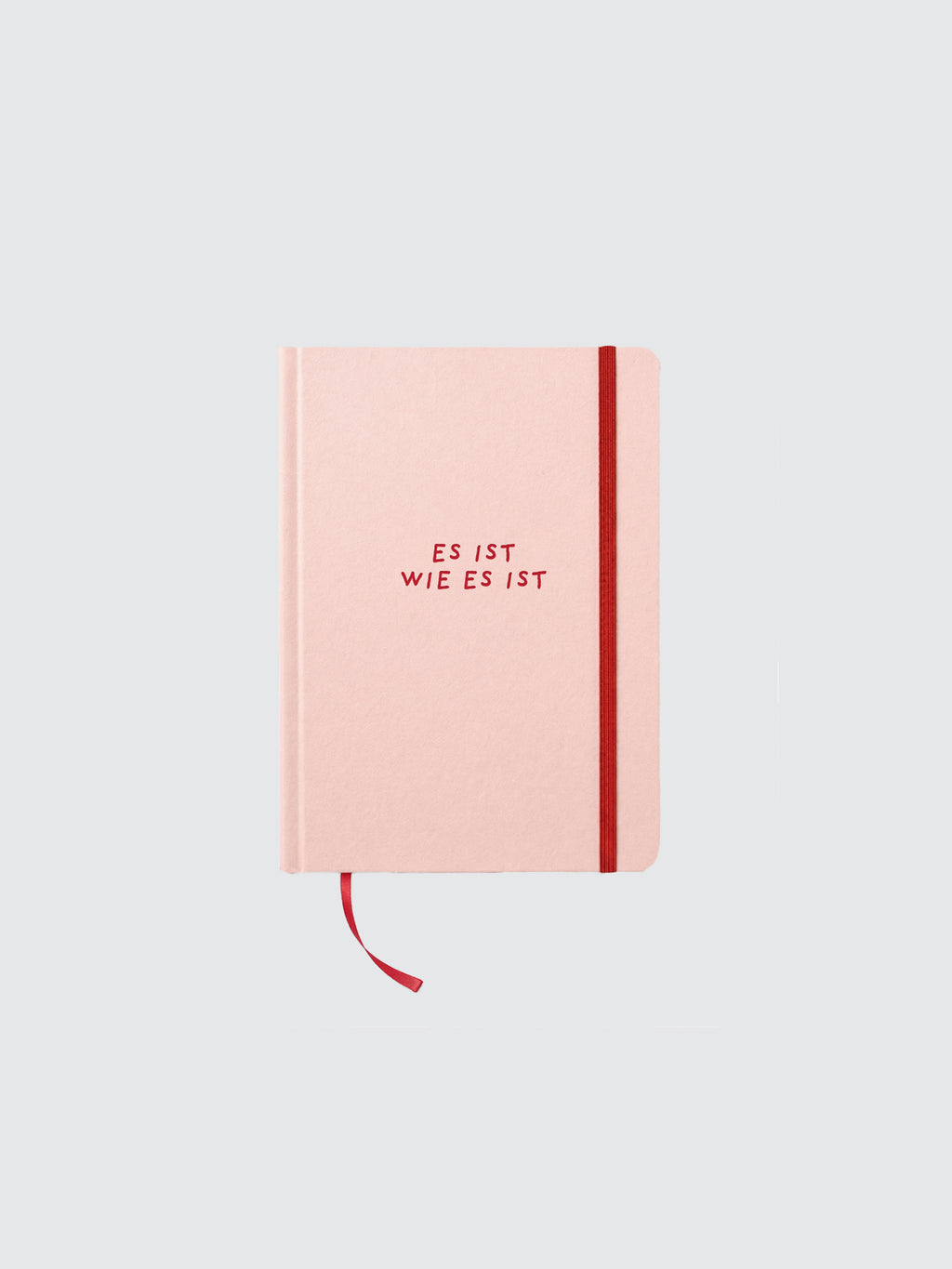 Rosa Hardcover-Notizbuch in minimalistischer Produktdarstellung auf hellem, neutralem Hintergrund. Auf dem Cover steht in roter Schrift „ES IST WIE ES IST“. Ein rotes Gummiband verläuft vertikal entlang der rechten Seite, dazu ein passendes rotes Lesebändchen unten. Das Notizbuch ist frontal ausgerichtet, symmetrisch positioniert und weich ausgeleuchtet.
